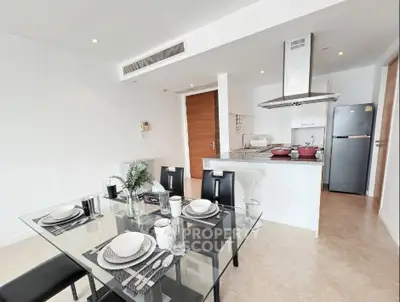 Modern open-plan kitchen and dining area with sleek glass table and contemporary appliances.