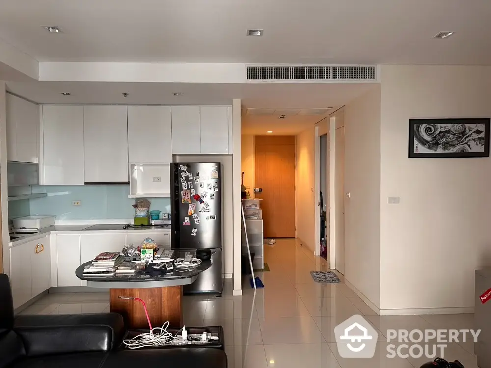 Modern kitchen with sleek white cabinets and stainless steel fridge in open layout apartment.