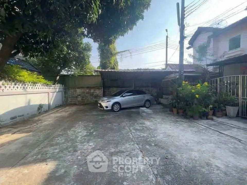 Spacious residential driveway with carport and lush greenery, ideal for family parking needs.
