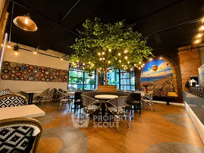 Chic cafe interior with stylish decor, vibrant wall art, and cozy seating under a faux tree with ambient lighting.