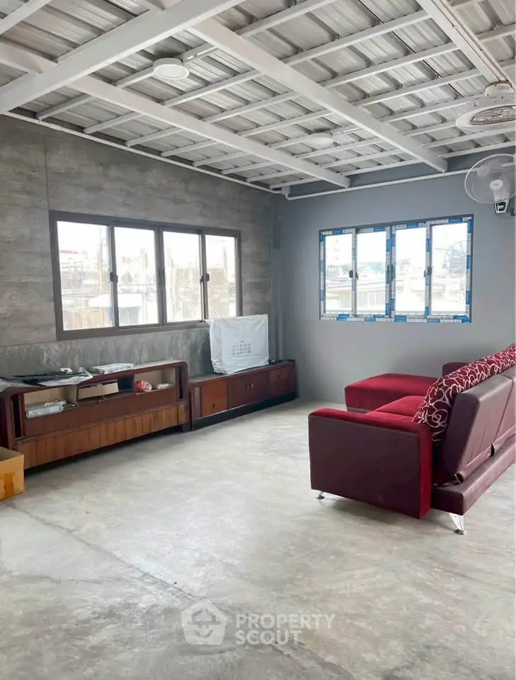 Spacious industrial-style living room with modern red sofa and large windows.