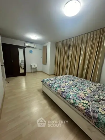 Spacious bedroom with floral bedding and elegant curtains, featuring ample storage and natural light.