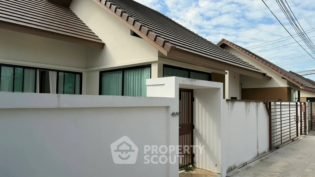 Modern single-story house with sloped roof and gated entrance in a suburban neighborhood.