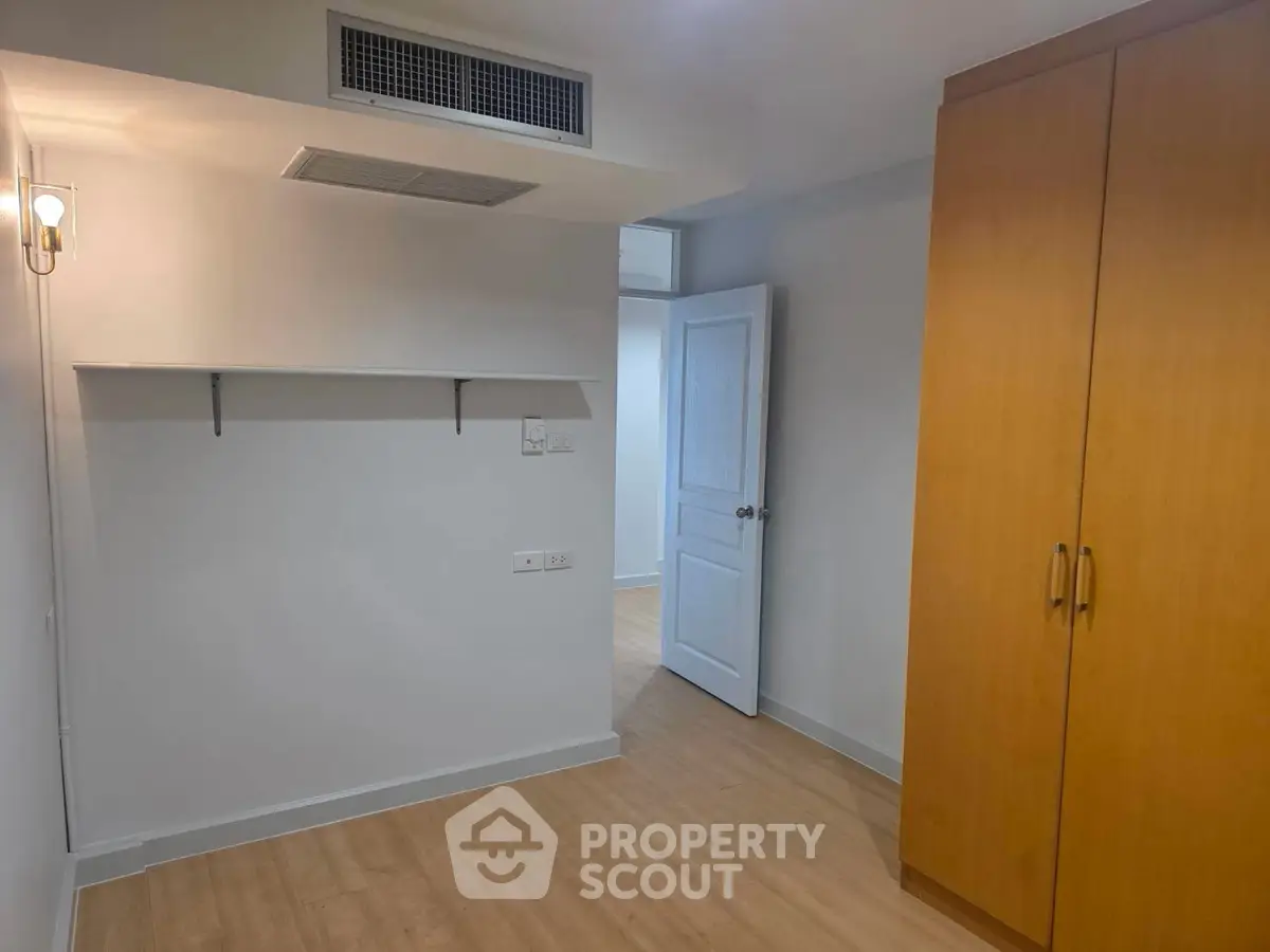 Spacious bedroom with wooden flooring and built-in wardrobe in modern apartment.