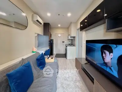 Modern living room with sleek design, featuring a cozy sofa, wall-mounted TV, and compact kitchen area.