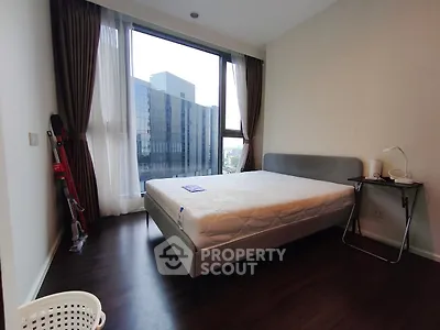 Modern bedroom with large window and city view, featuring a comfortable bed and sleek wooden flooring.