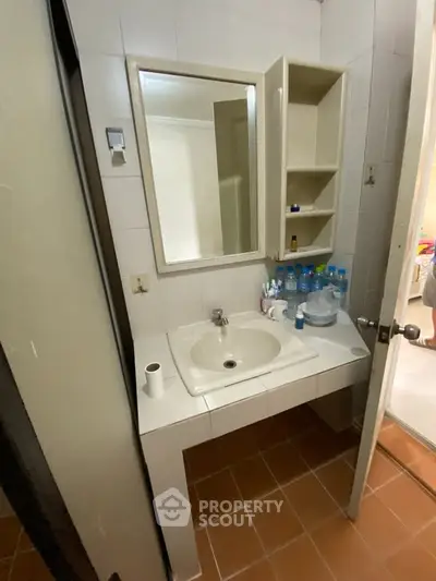 Compact bathroom with sink and mirror, featuring tiled floor and open shelving.