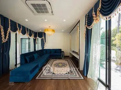 Luxurious living room with elegant blue drapes, plush sectional sofa, and chandelier lighting.