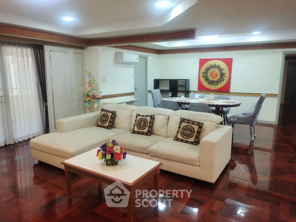 Spacious living room with elegant decor and dining area, featuring polished wooden floors and modern furnishings.