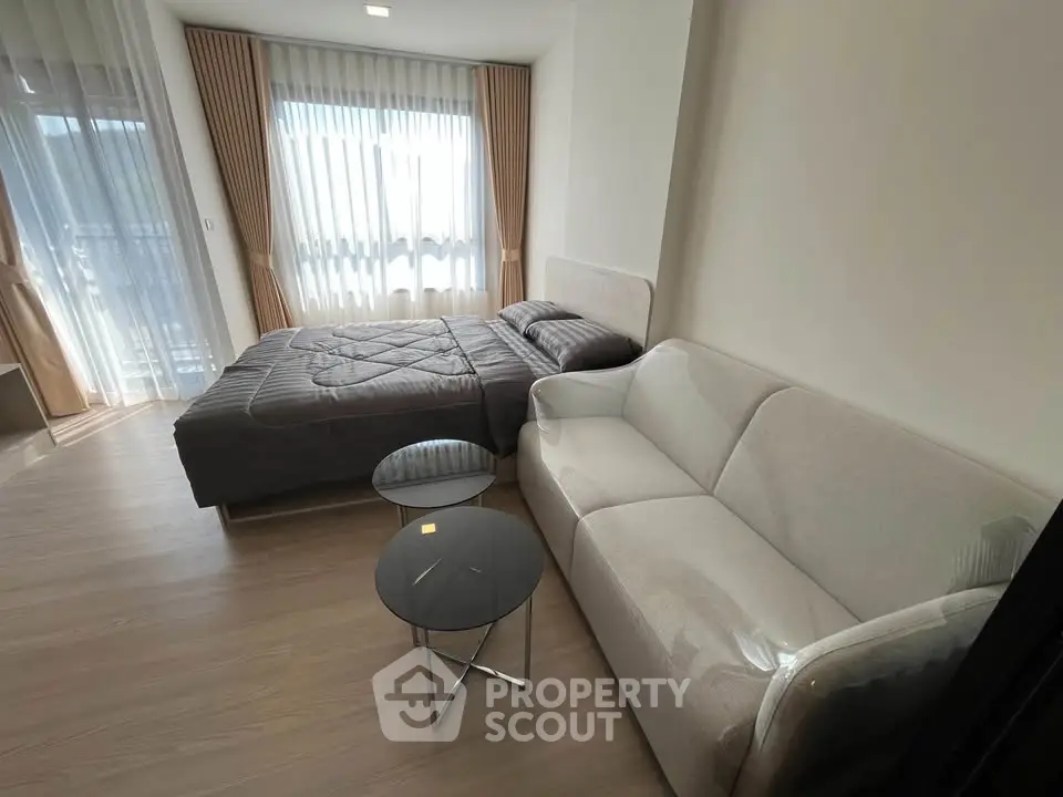 Modern bedroom with cozy bed and stylish sofa, featuring floor-to-ceiling windows and elegant curtains.