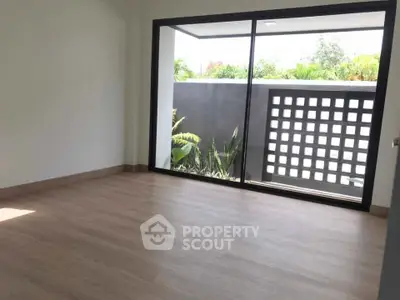 Spacious room with large sliding glass doors opening to a private garden view, featuring elegant wooden flooring.