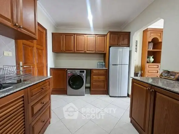 Spacious kitchen with wooden cabinets and modern appliances, featuring a washing machine and fridge.