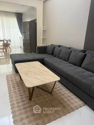 Modern living room with stylish gray sofa and elegant marble coffee table, open layout to dining area.