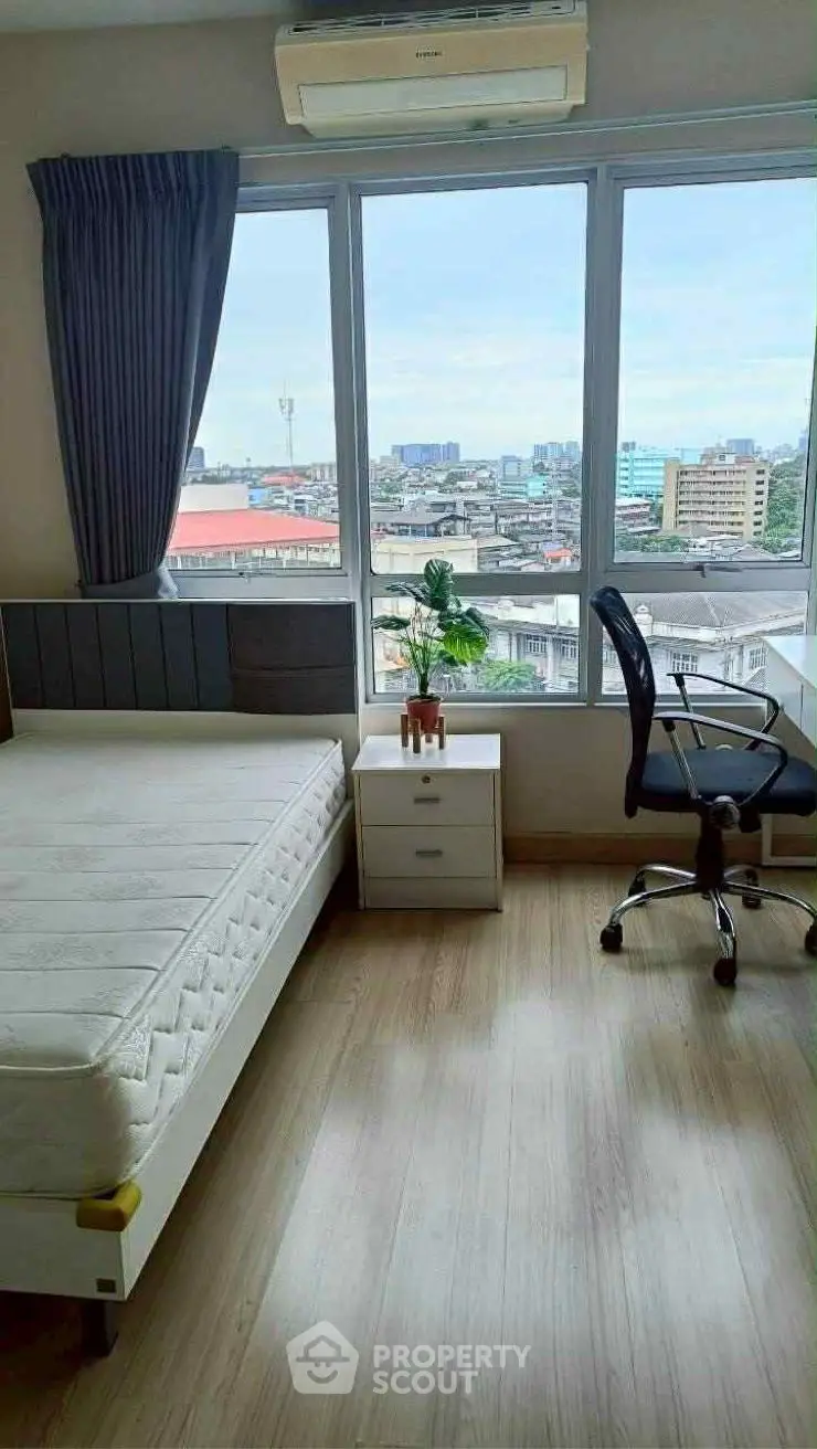 Modern bedroom with city view, featuring a bed, desk, and chair, ideal for urban living.