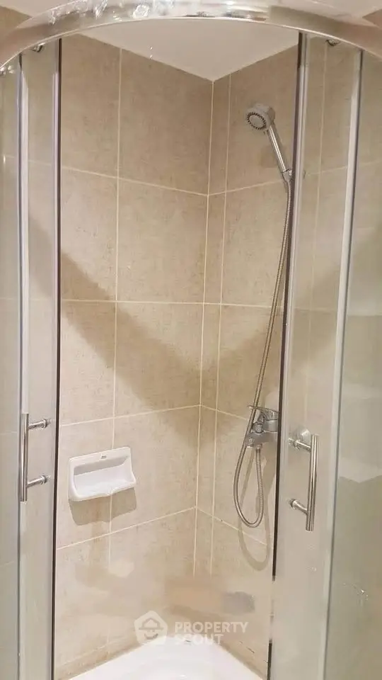 Modern bathroom with glass shower enclosure and beige tiled walls.