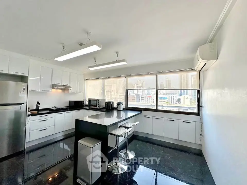 Spacious modern kitchen with city view, sleek black countertops, and white cabinetry in a high-rise apartment.
