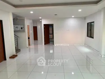 Spacious open-plan living area with glossy white tiles and modern lighting.