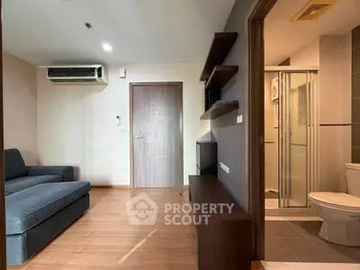 Modern apartment interior with cozy living room and adjacent bathroom, featuring sleek wooden flooring and stylish furniture.