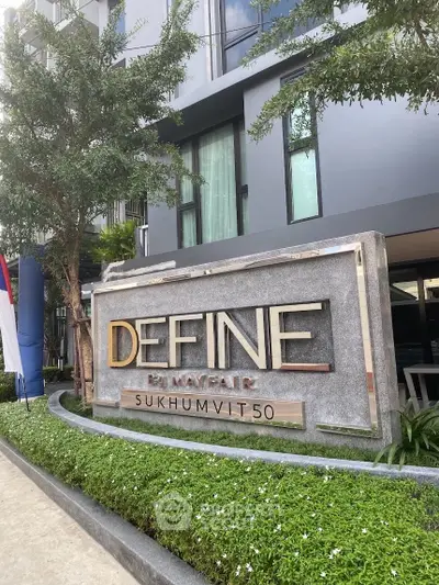 Modern condominium entrance with stylish signage and lush greenery at Define Sukhumvit 50.