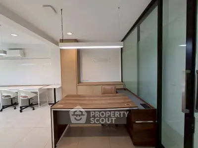 Modern office space with sleek wooden desk and glass partition, ideal for productivity.