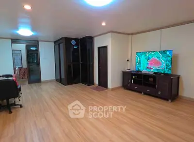 Spacious living room with modern decor and large TV, featuring sleek wooden flooring and ample natural light.