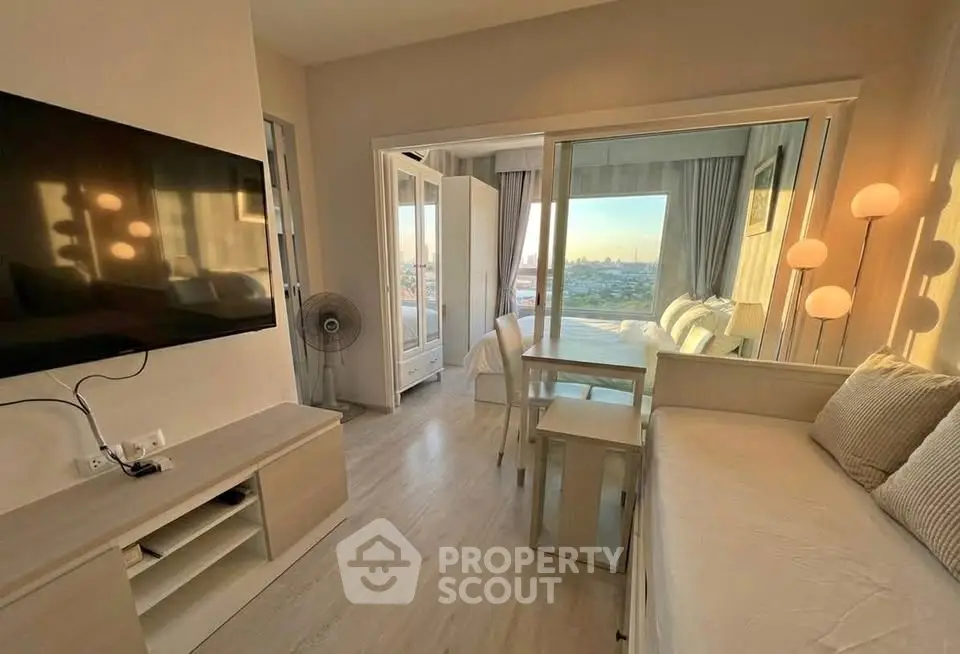Modern living room with large windows offering stunning city views, featuring cozy seating and a wall-mounted TV.