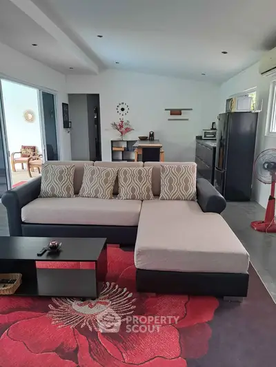 Modern living room with stylish sectional sofa and vibrant red floral rug, featuring open layout and sleek decor.