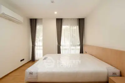 Spacious bedroom with large windows and modern minimalist design, featuring a comfortable bed and air conditioning.