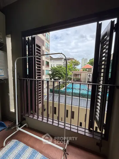 Urban apartment balcony with city view and pool, featuring open shutters and drying rack.