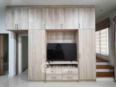 Modern living room with built-in wooden cabinetry and flat-screen TV, featuring sleek design and ample storage.