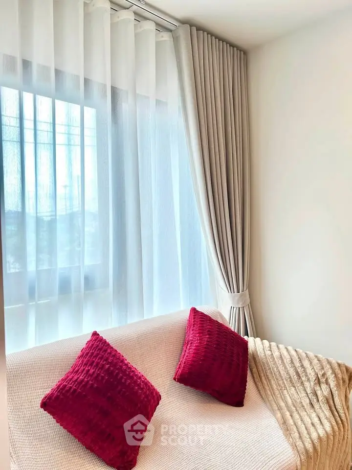 Cozy living room with elegant curtains and plush red cushions on a white sofa, perfect for relaxation.