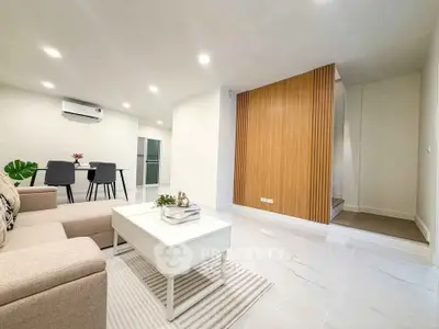 Modern living room with stylish decor and open dining area, featuring sleek furniture and bright lighting.