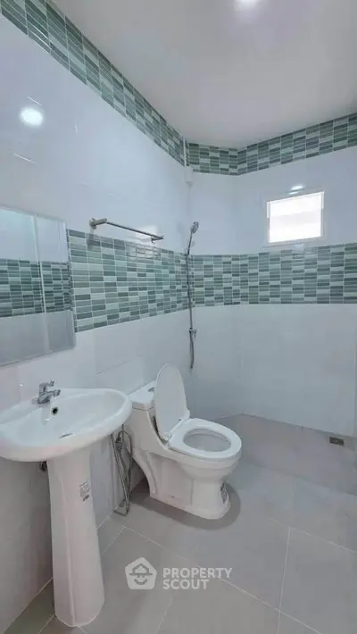 Modern bathroom with sleek white fixtures and stylish green tile accents.