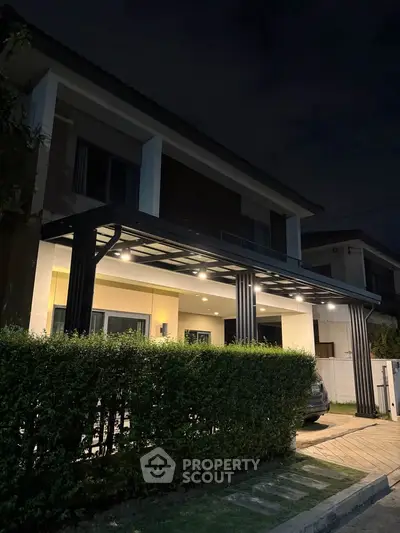 Modern two-story house with illuminated entrance and lush greenery at night