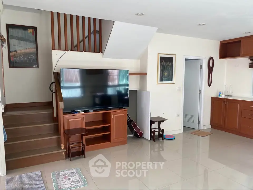 Spacious living room with modern TV setup and elegant wooden staircase