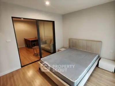 Modern bedroom with sliding glass doors leading to a cozy living area, featuring a stylish bed and wooden flooring.