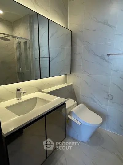 Modern bathroom with sleek fixtures and elegant marble tiles, featuring a stylish vanity and contemporary toilet design.