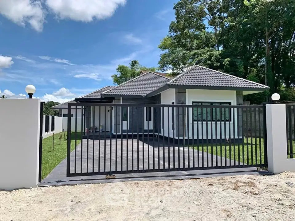 Modern single-story house with gated entrance and lush green surroundings.
