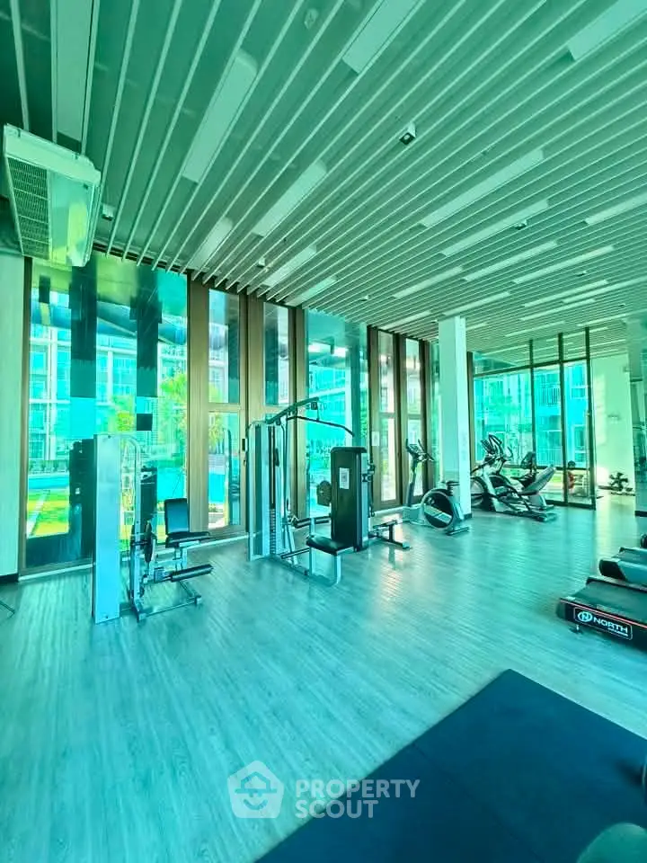 Modern gym with state-of-the-art equipment and floor-to-ceiling windows in luxury residential building.