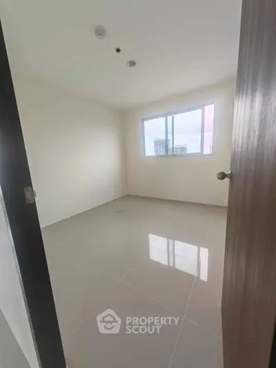 Spacious empty room with large window and glossy tiled floor in modern apartment.