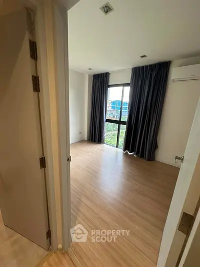 Spacious bedroom with wooden flooring and large window offering natural light.