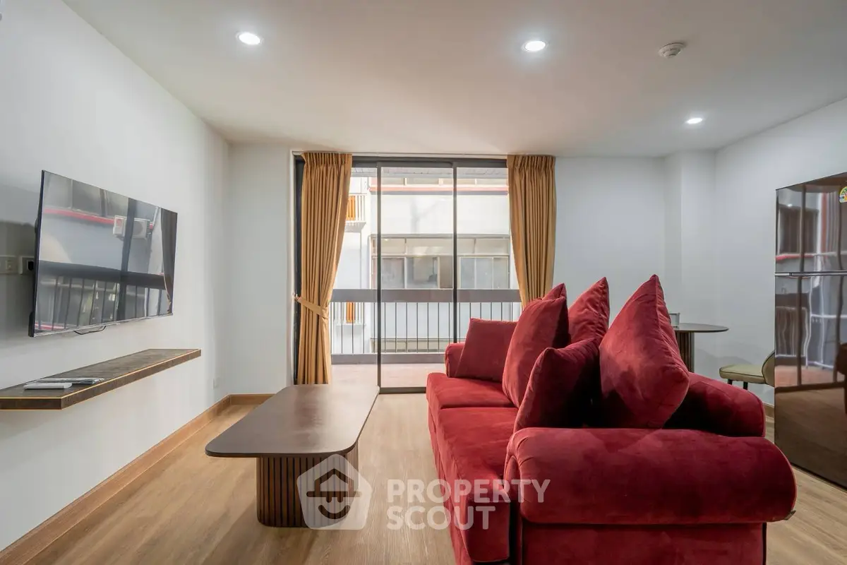 Modern living room with red sofa and wall-mounted TV, featuring large windows and wooden flooring.