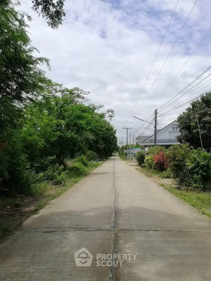 Scenic suburban street with lush greenery and residential houses under a cloudy sky.