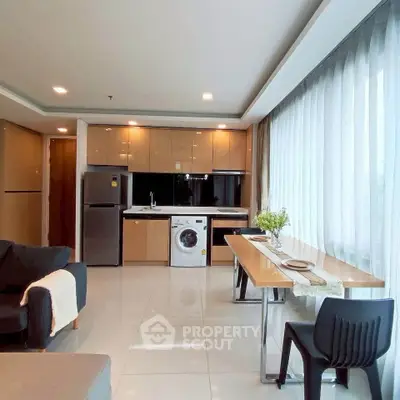 Modern open-plan living room with kitchen, featuring sleek appliances and large windows for natural light.