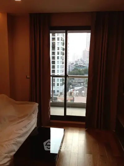 Cozy living room with city view from large window, featuring wooden flooring and elegant curtains.