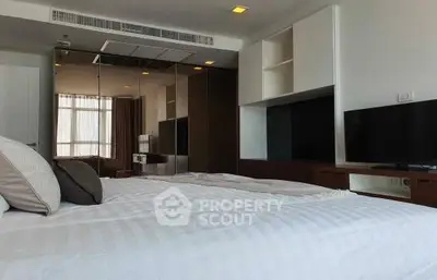 Spacious bedroom with modern design, featuring a large bed, two flat-screen TVs, and ample natural light from floor-to-ceiling windows.