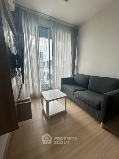 Cozy living room with modern sofa and TV, featuring floor-to-ceiling windows and wooden flooring.