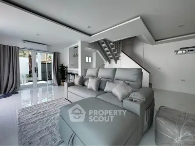 Spacious modern living room with sleek gray sofa and stylish staircase in a bright open layout.
