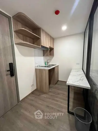 Modern compact kitchen with wood cabinetry and marble countertop in a stylish apartment.