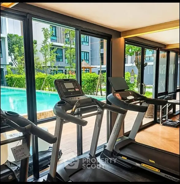 Modern gym with treadmills overlooking a pool and lush garden in a luxury apartment complex.